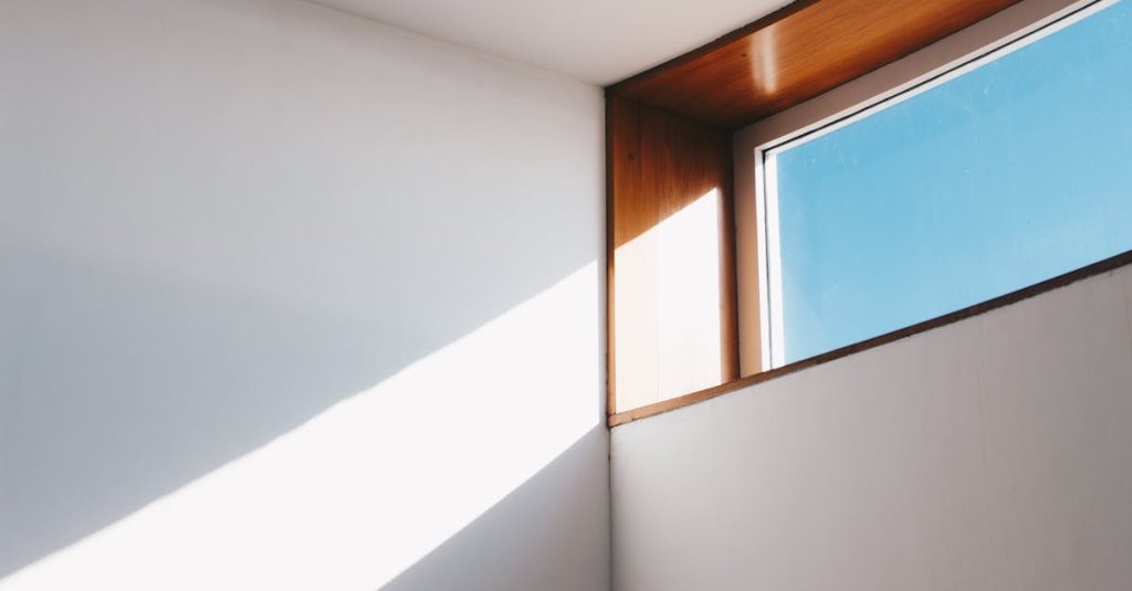 A minimalist interior showcasing sunlight streaming through a modern glass window against a blue sky.